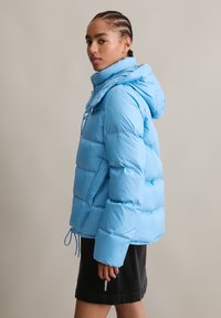 Puffjacke in Hellblau, mit Kapuze, elastischem Kordelzug in der Taille und vertikalem Steppmuster. Weicher, glänzender Stoff.