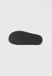 Black rubber shoe sole with a textured pattern featuring zigzag grooves and round edges, providing traction and durability.