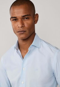 Svijetloplava košulja na dugih rukava izrađena od mješavine pamuka, s oštrim ovratnikom, suptilnom izvezenom logotipu i bijelim gumbima na prednjem dijelu.