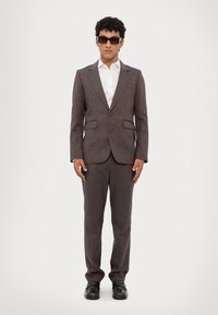 Bruin gestreept pak met een enkelvoudig gebreide blazer en bijpassende broeken, gecombineerd met een wit overhemd en zwarte schoenen.