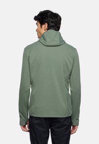 Giacca verde con cappuccio, maniche lunghe, texture liscia, vestibilità slim e dettagli di cucitura, abbinata a pantaloni scuri e morbidi.