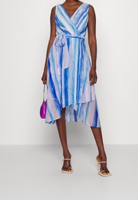 Vestido envolvente en rayas azules y lavandas, corto en la parte delantera y más largo en la parte trasera, con cintura anudada y tejido ligero.