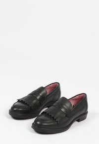 Een paar zwarte leren loafers met gelaagde franjes bovenop en een roze binnenvoering op een witte achtergrond.