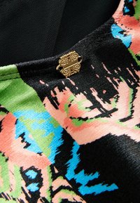 Kleurrijke stof met een zwarte basis, versierd met bloemenpatronen in roze, groen en blauw. Gouden decoratieve sluiting bij de hals.
