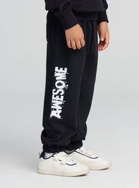 Czarne spodnie dresowe z napisem "AWESOME" w białym kolorze na lewej nogawce, wyposażone w ściągacze na końcach i boczne kieszenie. Do tego białe trampki.