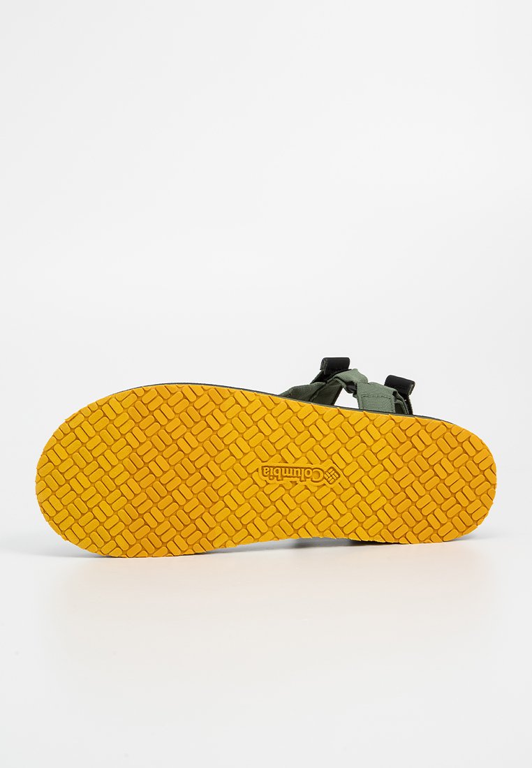 Sandały z teksturowaną żółtą podeszwą z logo Columbii oraz regulowanymi zielonymi paskami z tkaniny widocznymi na górnej stronie.