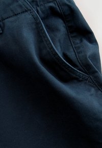Dark navy fabric showing a smooth texture with visible stitching details and a pocket outline, indicating a pair of pants or shorts.