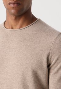 Beiger Pullover mit Rundhals, aus einem strukturierten Strickmaterial, mit einem schlanken Schnitt und sichtbaren Nähten entlang der Kanten.