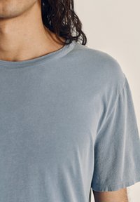 Light blue, short-sleeved t-shirt made of soft fabric, featuring a round neckline and subtle texture. Clean seams and no visible patterns.