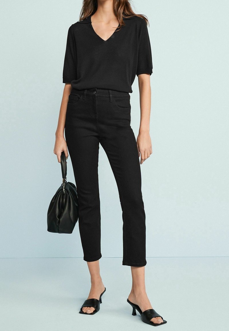 Top noir à manches courtes avec un décolleté en V, associé à un jean skinny noir taille haute. Des mules noires à bouts ouverts et un sac à main noir complètent le look.