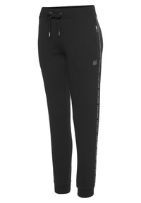 Schwarze Jogginghose aus weichem Stoff, mit einem Kordelzugbund, seitlichen Reißverschlusstaschen und einem Logo-Print an der Seite. Enganliegende Bündchen.