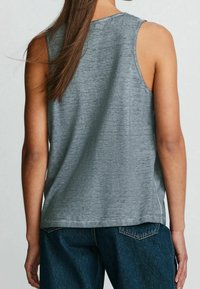 Grå ærmeløs top med en let tekstureret stof, rund hals og sideslidser, kombineret med mørkeblå jeans med lige ben.