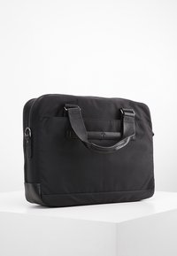 Svart laptopväska gjord av slitstark tyg med läderdetaljer. Har två ovandelshandtag, dragkedjestängning och en platt rektangulär form.