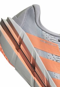 Grauer und orangefarbener Sportschuh mit strukturiertem Mesh-Obermaterial, auffälligen orangefarbenen Streifen und dicker Sohle, gekennzeichnet mit "Repetitor" und "Adistar BYD."