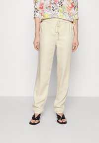 Crème satijnen broek met een elastische tailleband en een trekkoord. Relaxte pasvorm, taps toelopend pijp, gecombineerd met zwarte geknoopte sandalen.