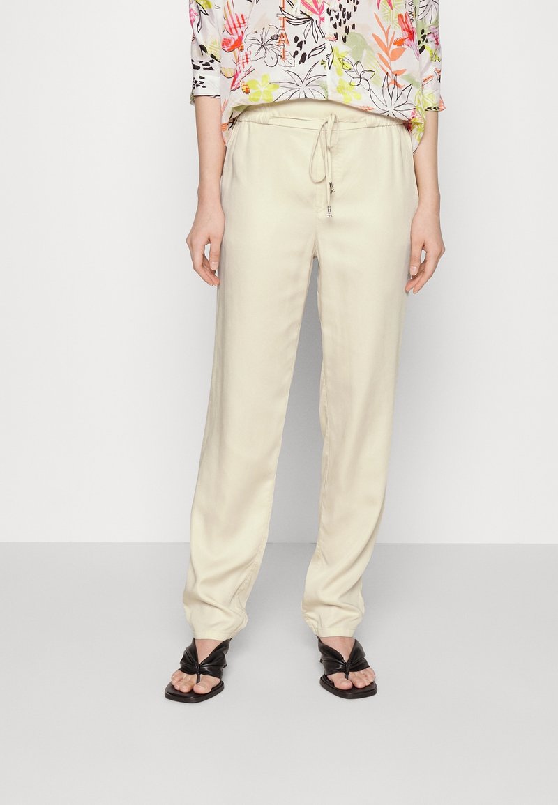 Crème satijnen broek met een elastische tailleband en een trekkoord. Relaxte pasvorm, taps toelopend pijp, gecombineerd met zwarte geknoopte sandalen.