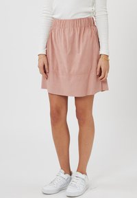Gonna rosa in morbida suede con vita elastica, lunghezza al ginocchio, con orlo svasato e dettagli di cucitura minimal. Indossata con sneakers bianche.