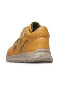 Scarpa gialla in pelle con finitura testurizzata, cinturino in velcro e suola in gomma grigia caratterizzata da un motivo a battistrada. Logo verde sul lato.