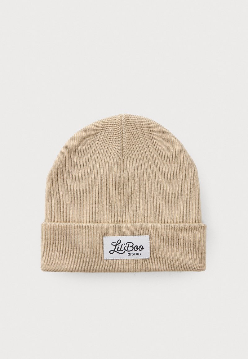 Pleteni zimski šešir u svijetloj bež boji s preklopom i bijelom etiketom na kojoj piše "Lil' Boo Copenhagen" crnim rukopisom.