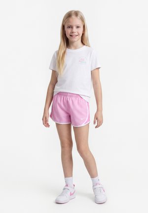 Jeune fille debout, portant un t-shirt blanc, un short de sport rose, des chaussettes blanches et des baskets blanches avec des touches roses.