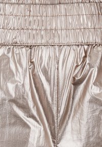 Metallisch beige stof met een gekreukt textuur, voorzien van een elastische tailleband en geplooide details.
