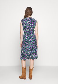 Krótka sukienka w kwiaty z ciemnozielonym tłem, ozdobiona fioletowymi, różowymi i białymi kwiatami. Posiada dopasowaną talię i rozkloszowany dół, zestawiona z beżowymi botkami.