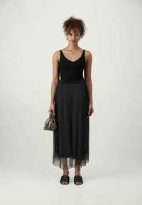 Top preto canelado combinado com uma saia maxi preta, leve e plissada. Os acessórios incluem uma pequena mala castanha e sandálias pretas de tecido.