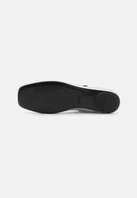Suela de zapato negra con una superficie lisa y una ligera curvatura. Presenta un área de talón reforzada y un sutil logo cerca del arco. Diseño plano.