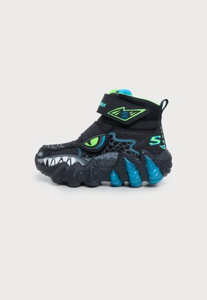 Basket montante noire pour enfant, au style monstre, avec un œil vert, des dents blanches, des piquants bleus et une bride à fermeture autoagrippante.