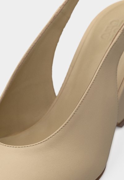 Μπεζ δερμάτινα γόβες με λουράκι στο πίσω μέρος, ψηλό χοντρό τακούνι και στρογγυλεμένη μύτη, εμφανιζόμενα σε κλειστό πλάνο με ορατή ραφή.