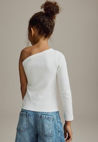 Vit, ribbad långärmad topp med en asymmetrisk axeldesign, i kombination med högmidjade denimshorts med två bakfickor.