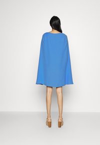 Blue, flowing cape dress with a round neckline. Short sleeves provide coverage. Worn with beige heeled sandals, smooth texture throughout.