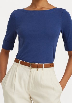 Blauw aansluitend T-shirt met korte mouwen gecombineerd met witte hoge taille broek en een bruine leren riem met gouden gesp.