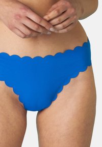 Parte inferiore di bikini blu realizzata in un tessuto morbido con un design a bordo ondulato. Adatta per costumi da bagno, enfatizza una silhouette senza cuciture.