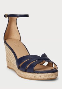 Tengerészi bőr wedge sarok szandál, bokapánttal, nyitott orral és több keresztezett pánttal. A kenderrel bevont sarok texturált kontrasztot nyújt.