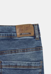 Primer plano de unos vaqueros de mezclilla azules que muestra el bolsillo trasero y una etiqueta de cuero marrón con la marca "Blue Effect Premium Jeans".