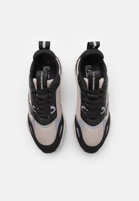 Zwarte en beige sneakers met meshnaden, een gladde textuur, ontworpen met een prominent logo, platte veters en een trekhaak op de hiel.