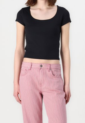 Kobieta nosząca czarny krótki crop top i wysokie spodnie w różowo-białe pionowe paski na białym tle.
