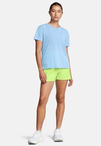 Camisa de manga corta azul claro combinada con pantalones cortos verdes brillantes. Los zapatos son de estilo atlético en blanco. Diseño simple con textura suave.