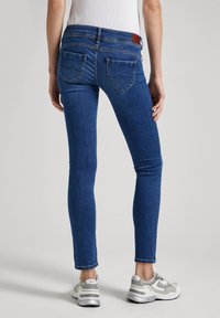 Smal jeans i mörkblå denim med medelhög midja, detaljerad sömnad på bakfickorna och en slät yta. Bärs med sneakers.