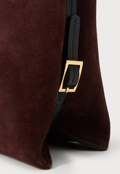 Burgundy mockaskinnväska med ett svart läderrem, som har ett spänne i guldmetall och en slät yta, vilket framhäver en modern, strukturerad form.