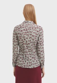 Blusa a maniche lunghe in tessuto verde chiaro con un motivo animale rosso ripetuto. Dettagli arricciati in vita e colletto.