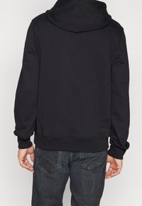 Černá mikina s klokaní kapsou, žebrovanými manžetami a lemem. Vyrobena z měkké tkaniny, má minimalistický design bez viditelných log.