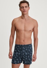 Marine zwempantalons met een speels patroon van ski- en wintersporticonen. Elastische tailleband met een trekkoord voor een verstelbare pasvorm.