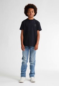 Sort bomuld T-shirt med korte ærmer og et lille rundt logo på brystet, kombineret med lyseblå jeans og hvide sneakers.