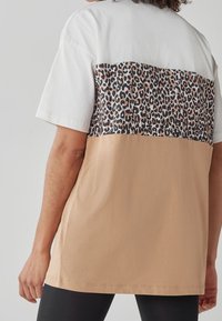 Kortærmet T-shirt med hvid øverdel, leopardprintet midtersektion og tan nederste sektion. Glat bomuldsstruktur gennem hele. 
