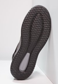 Suola nera di scarpa con una texture ondulata, caratterizzata da una sezione grigia etichettata "SKECHERS" e una forma liscia e arrotondata.