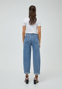 Jeans de mezclilla de tiro alto, de color azul claro, con un corte relajado, puños doblados y dos bolsillos traseros. Combinados con una camiseta blanca y sandalias de tacón negras.