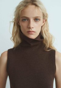 Rjava brezrokavna turtleneck pulover iz mehkega pletenja. Ima visok ovratnik in prilegajoč dizajn, z gladko teksturo in diskretnimi rebrastimi detajli.