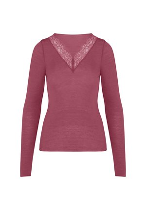 Vrouw die een mauve top met lange mouwen draagt, tilt deze licht op om bijpassend mauve ondergoed te tonen tegen een effen lichte achtergrond.